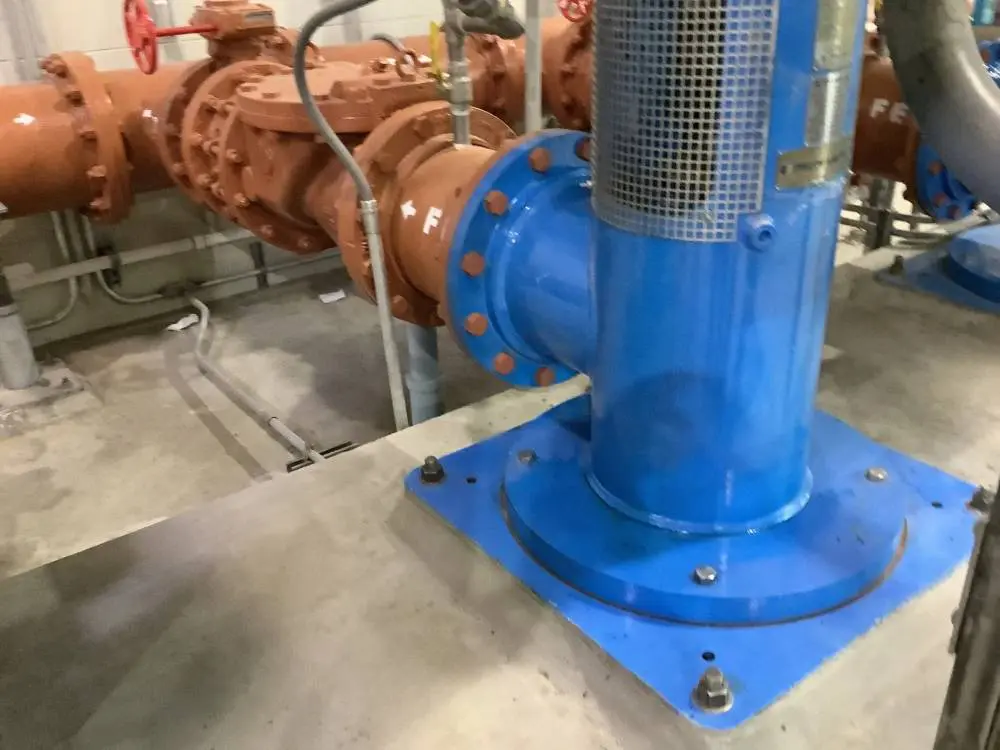 A blue pump sitting next to pipes in an industrial setting.